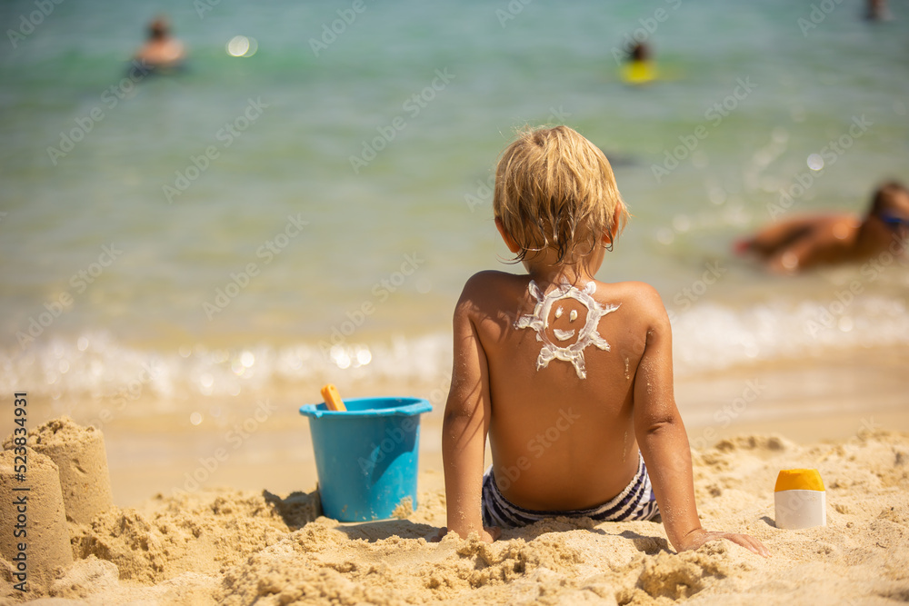 Happy child, blond boy on the beach with applied sun screen, enjoying summer, playing Happy child, blond boy on the beach with applied sun screen, enjoying summer, playing