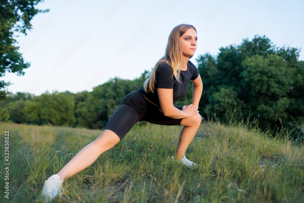 athletic blonde goes in for sports in the park performs exercises to stretch the muscles of the legs athletic blonde goes in for sports in the park performs exercises to stretch the muscles of the legs