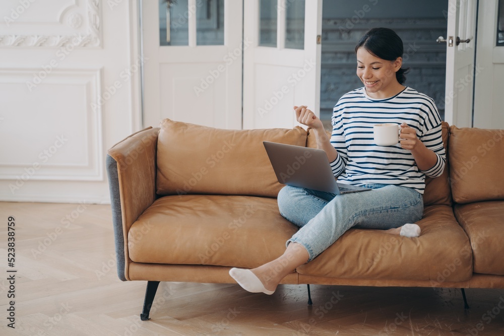 Relaxed woman is working from home and has coffee. Lady is sitting on couch and has online meeting. Relaxed woman is working from home and has coffee. Lady is sitting on couch and has online meeting.