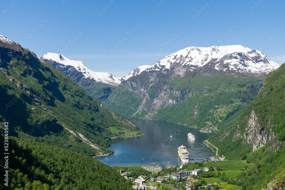 Geiranger Fjord and village Geiranger surrounded by high green and snowy mountains in Norway.