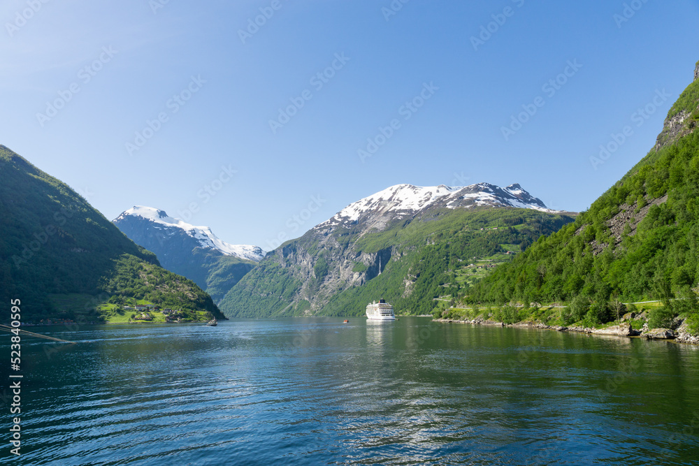 Geiranger Fjord surrounded by high green, snow-capped mountains and a ship.
