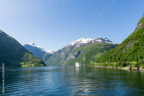 Geiranger Fjord surrounded by high green, snow-capped mountains and a ship.