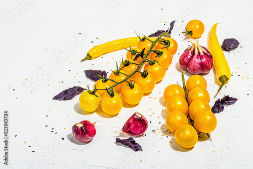 Culinary background with ripe vegetables. Yellow tomato cherries, chili pepper, garlic, purple basil. Fresh vegetables on white putty background, modern hard light, dark shadow, flat lay photo