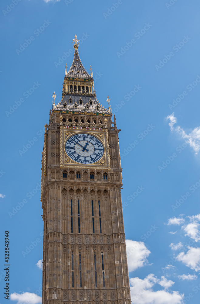 London, UK - July 4, 2022: Big Ben tower top half against blue cloudscape shows golden trim, clock and spire.