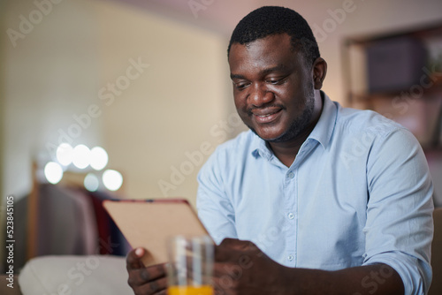Portrait of positive Black man reading news article on tablet computer at home