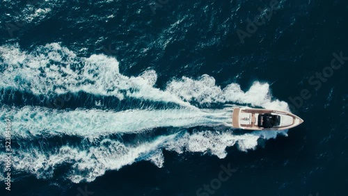 Top view slow motion drone shot of luxury motorboat in ocean waters near marina. Panning shot of yacht swim and raise waves in open blue waters. Amazing epic background over waves in sea