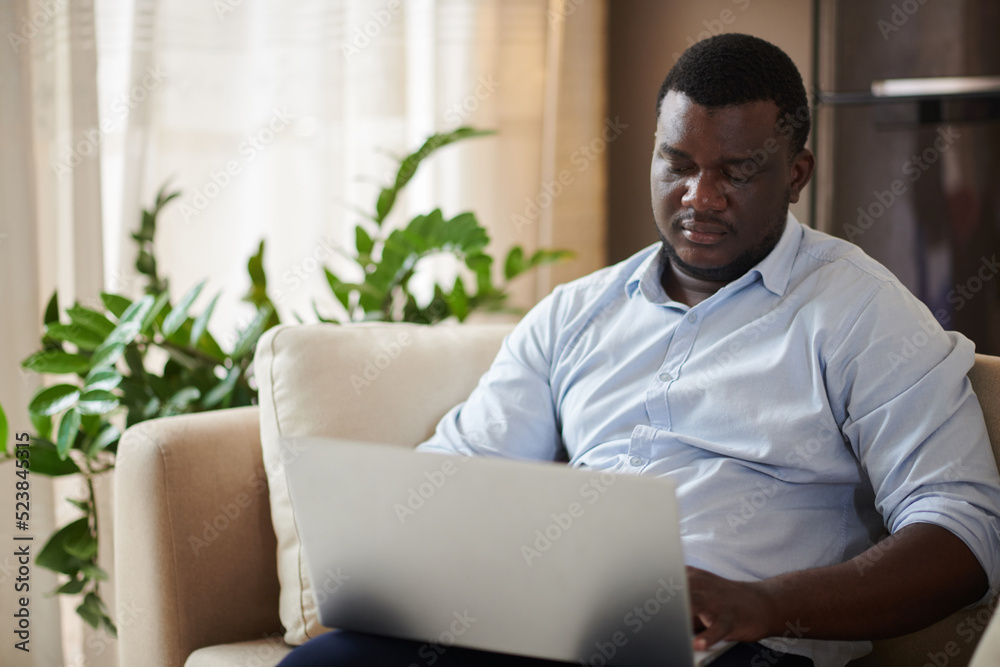 Portrait of Black businessman sitting on couch when working on laptop at home Portrait of Black businessman sitting on couch when working on laptop at home