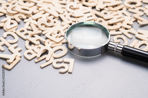 Magnifying glass on the pile of wooden English alphabets, glossary, and keyword, search the right word for communication, learning English concept photo
