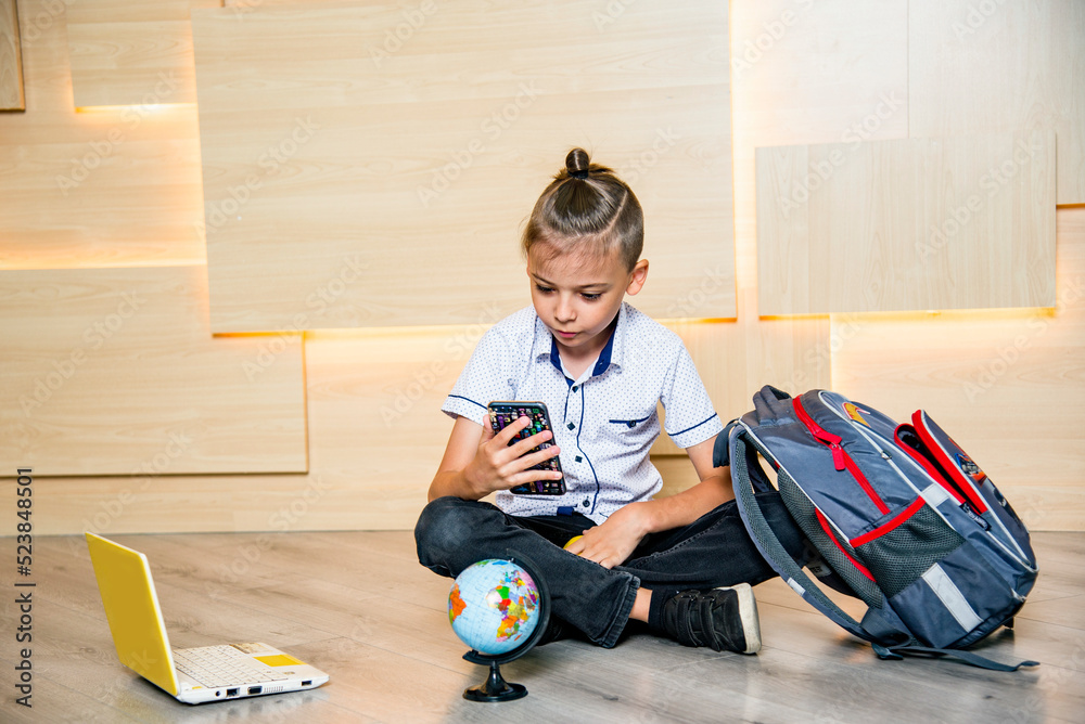 funny boy sitting on the floor and speaking by phone with apple, globe,  schoolbag and laptop. Back to school Stock Photo | Adobe Stock