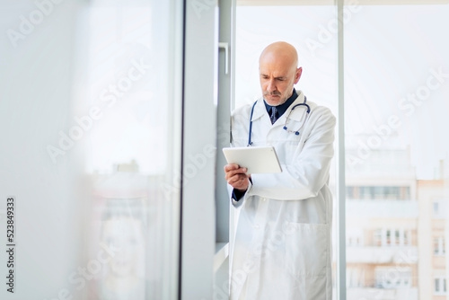 Male doctor using digitla tablet while standing on clinic's foyer