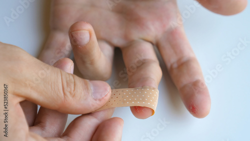  Male applying band aid patch to injured sore fingers. Man putting medical adhesive bandage tape sticking plaster on cuts wound on finger. First aid after accident, self cure concept. Close-up.