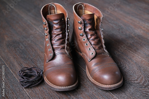 leather work boots without laces next to shoelaces on wooden floor, shoes are prepared to care and cleaning