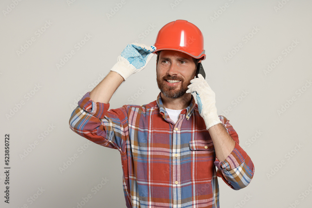 Professional builder in hard hat talking on phone against light background Professional builder in hard hat talking on phone against light background