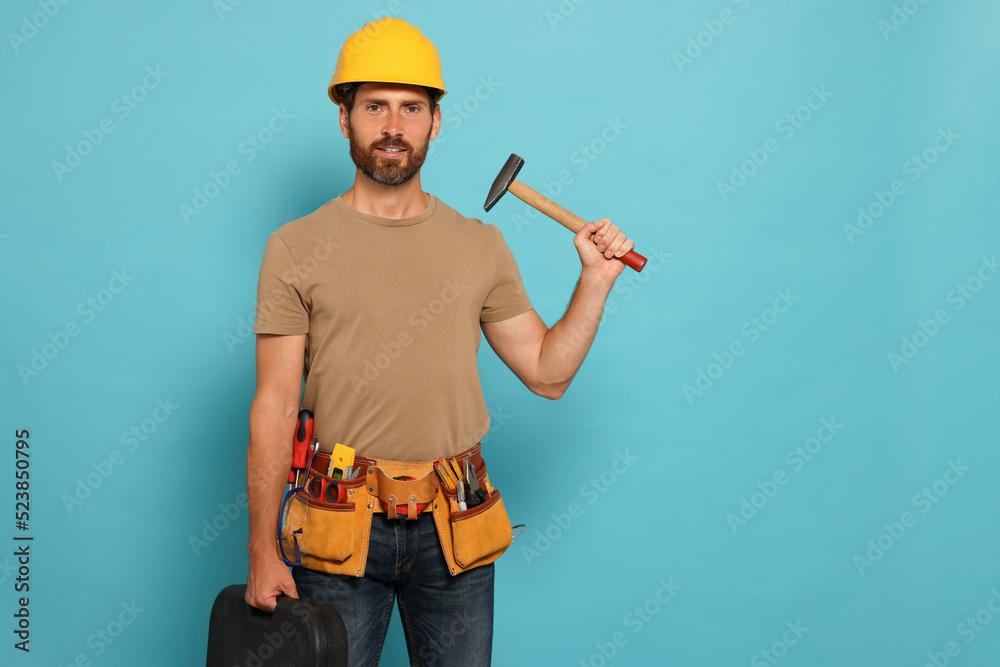 Professional builder in hard hat with hammer and tool belt on light blue background, space for text Professional builder in hard hat with hammer and tool belt on light blue background, space for text