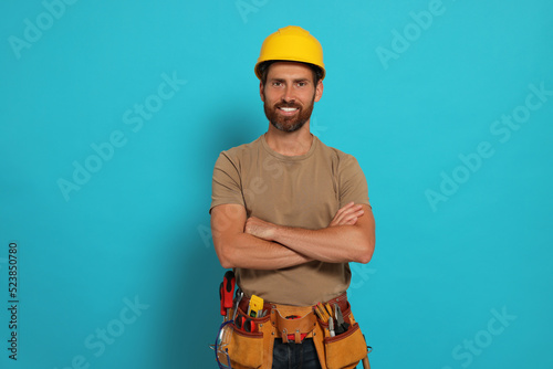 Professional builder in hard hat with tool belt on light blue background © New Africa