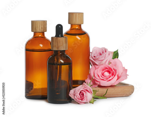 Bottles of essential rose oil and flowers on white background