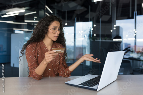 Upset business woman in modern office trying to make a purchase in an online store, got an error and rejection, business woman using laptop and holding a bank credit card