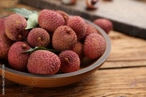Fresh ripe lychee fruits in bowl on wooden table, closeup