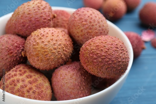 Fresh ripe lychee fruits in bowl on blue table, closeup