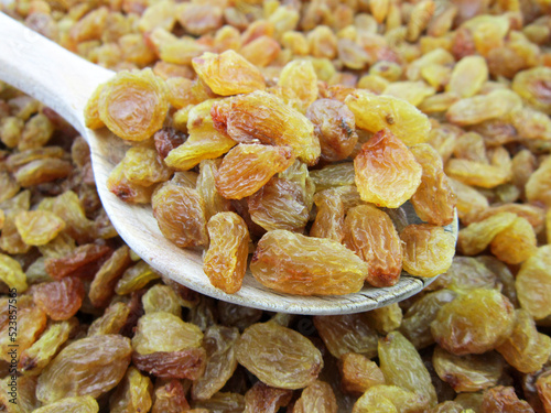  yellow golden raisins in wooden spoon