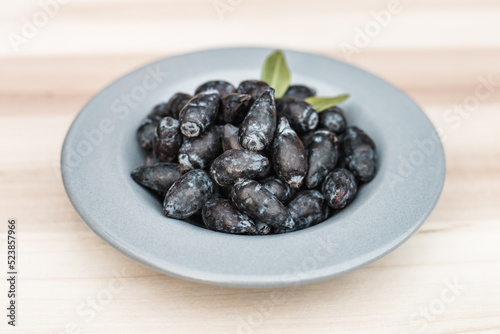 Freshly picked haskap berries / honeysuckle (Lonicera caerulea) on a gray plate, on a wooden board, with green leaves. Organic healthy berries full of vitamins.