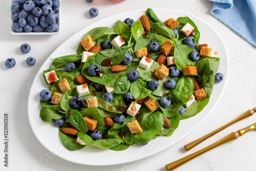 Blueberry salad with spinach, almonds, croutons and feta cheese оn white plate with fresh berries on background. Top view.