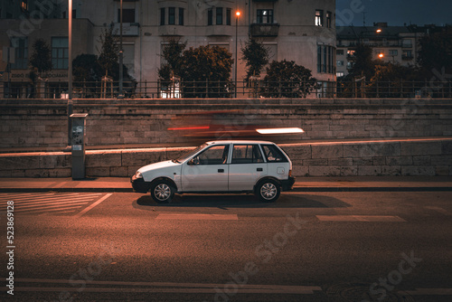 Classic European hatchback parked under street light with can speeding past behind it making motion blue, in Budapest, Hungary 