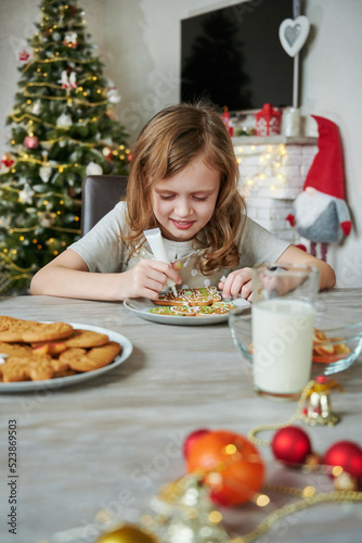 Girl is decorating Christmas cookies. Child is preparing holiday food. Merry Christmas and Happy Holidays. Children's creativity and learning process.