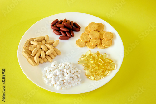 A handful of pills, capsules and multi-colored tablets on a plate next to cutlery. Taking medication. Pills instead of food. The concept of vitamins instead of food