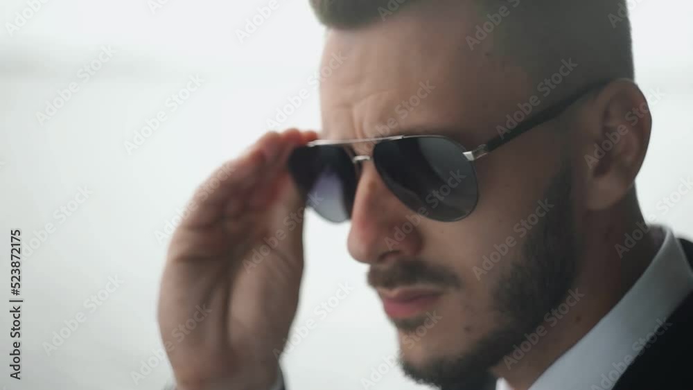 Close up of bearded handsome businessman in suit puts on his sunglasses Close up of bearded handsome businessman in suit puts on his sunglasses