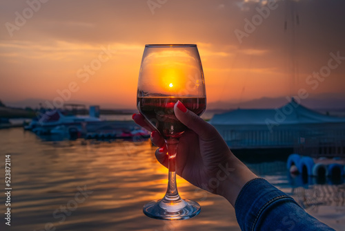 a girl holds in her hand rose wine or champagne in a glass on the seashore in the evening at sunset