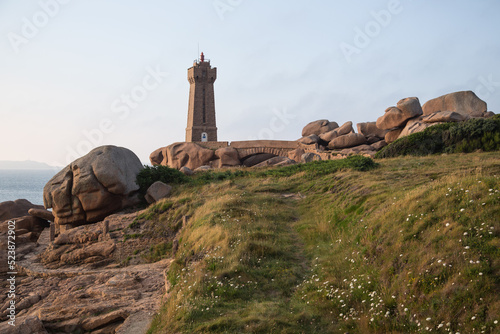 The lighthouse Men Ruz with bridge towering the extraordinarily colored and fantastically shaped rock formations at the walking trail dotted with wild flowers - pink granite coast in Brittany, France © blickwinkel2511