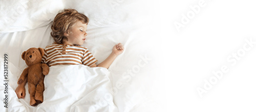Banner with top view of cute little baby sleeping sweetly with bear toy on white clean bed clothes in his cozy bed at home