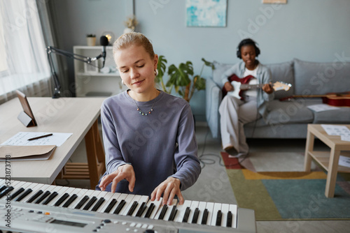 Portrait of blonde young woman playing synthesizer at home and composing music , copy space photo