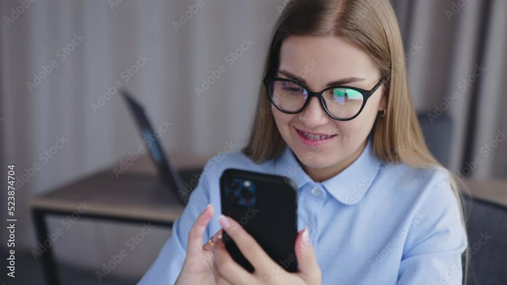 Beautiful young blonde woman in glasses holding phone in front of her face. Lady smiling and taking selfie on her smartphone. Close up. Beautiful young blonde woman in glasses holding phone in front of her face. Lady smiling and taking selfie on her smartphone. Close up.