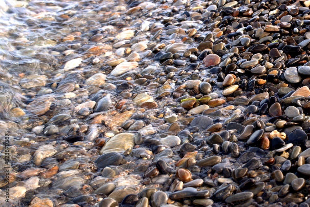 A pure transparent sea wave rolls over the rocky pebble shore, the concept of rest and travel, tranquility, relaxation and reflection on a warm summer day, close-up. A pure transparent sea wave rolls over the rocky pebble shore, the concept of rest and travel, tranquility, relaxation and reflection on a warm summer day, close-up.