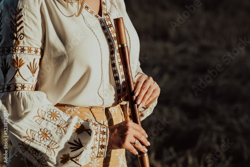 Woman holding woodwind wooden flute - ukrainian telenka or tylynka. Folk music concept. Musical instrument. Musician in traditional embroidered shirt - Vyshyvanka.