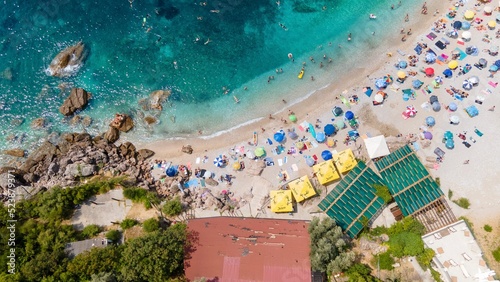 Aerial view from flying drone. People relax on a beautiful beach surrounded by greenery and rocks