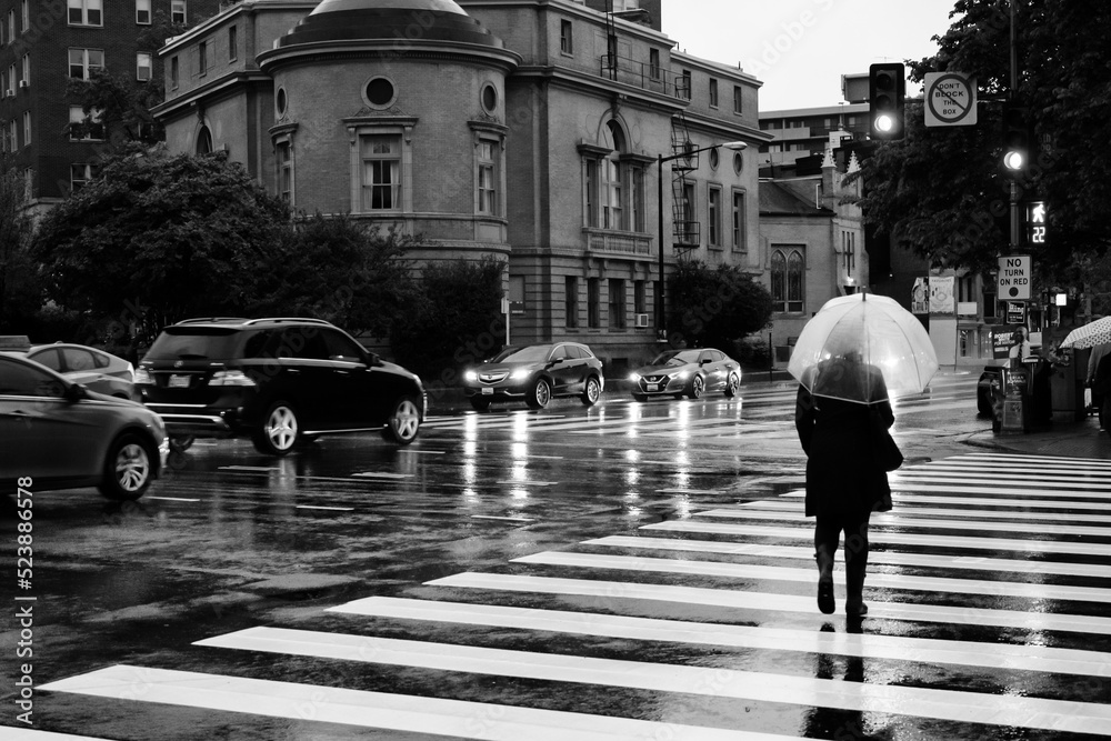 B&W image of a person walking in the rain with a bubble umbrella on the street in Washington DC.