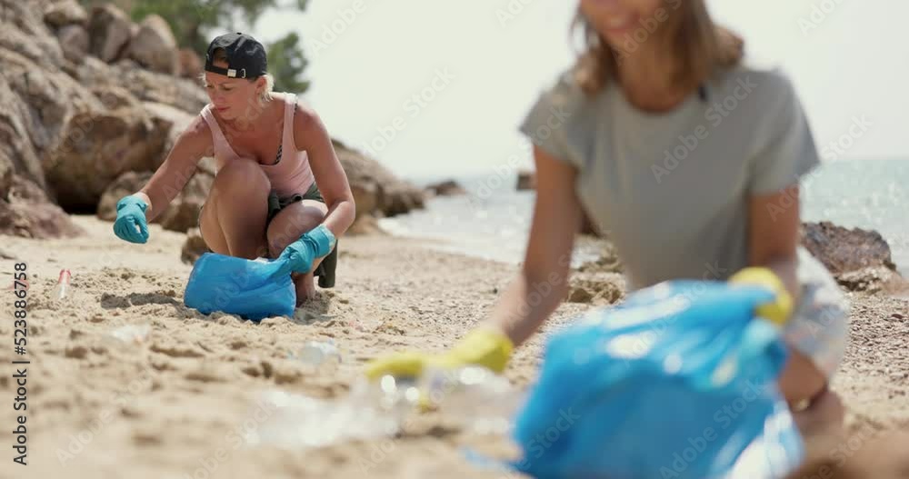 Mother and daughter volunteers cleaning the sea beach by collecting garbage into plastic bag. Mother and daughter volunteers cleaning the sea beach by collecting garbage into plastic bag.