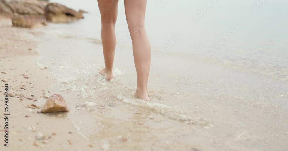 Close-up of an unrecognizable female teenager's legs is walking along the empty sandy sea beach. Close-up of an unrecognizable female teenager's legs is walking along the empty sandy sea beach.