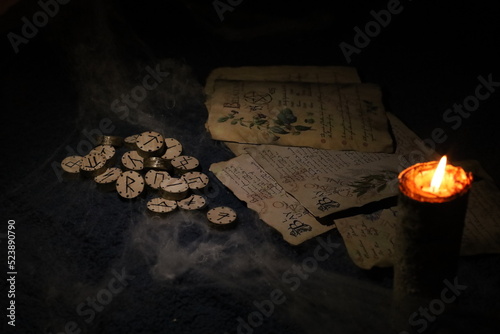 Fotografía On Halloween night, in the light of a burning candle, runes and old sheets of a book are wrapped in cobwebs