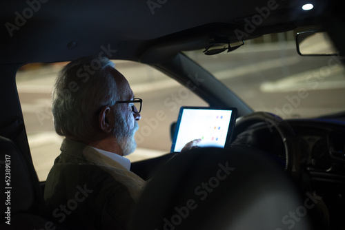 Senior man sitting in the car and using navigation system on parking lot at night 