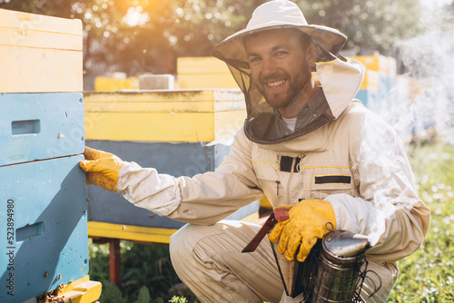 Portrait of a happy male beekeeper working in an apiary near beehives with bees. Collect honey. Beekeeper on apiary. Beekeeping concept.
