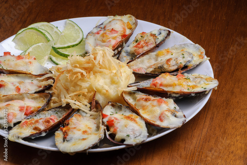 Baked mussels au gratin with mashed potatoes on a white plate on wooden table. Brazilian seafood. photo