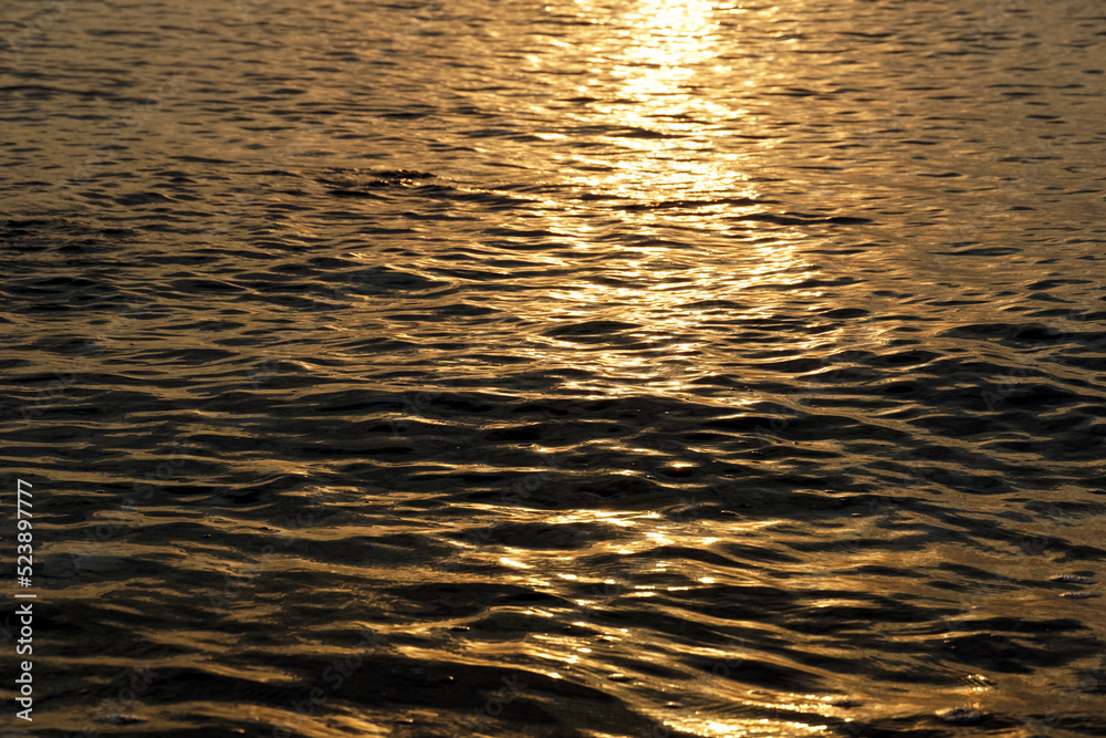 The rippled and wavy surface of the sea in golden color with the shine of the sun rays on the surface