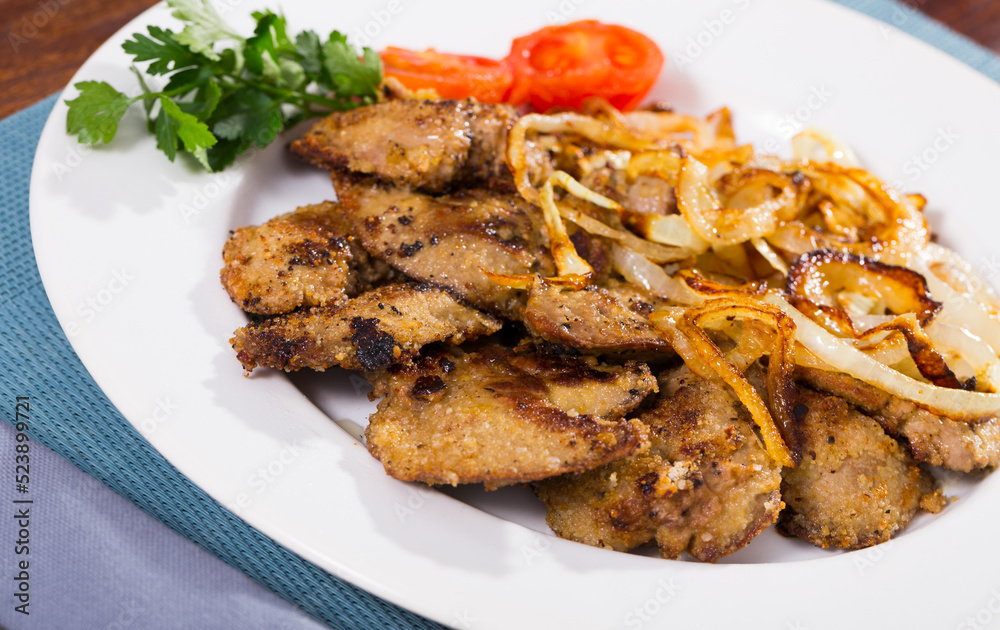 Fried rabbit liver served on white plate with grilled onion and cherry tomatoes