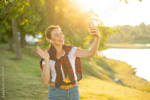 Attractive woman smiling happy doing video call using smartphone at the park. Girl wave hand having videocall online © Ivan