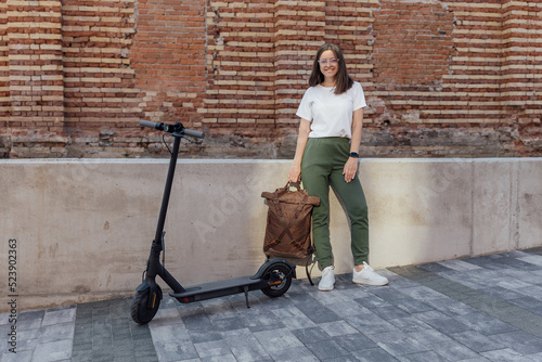 Young woman in white sneakers standing near electric scooter in city urban street