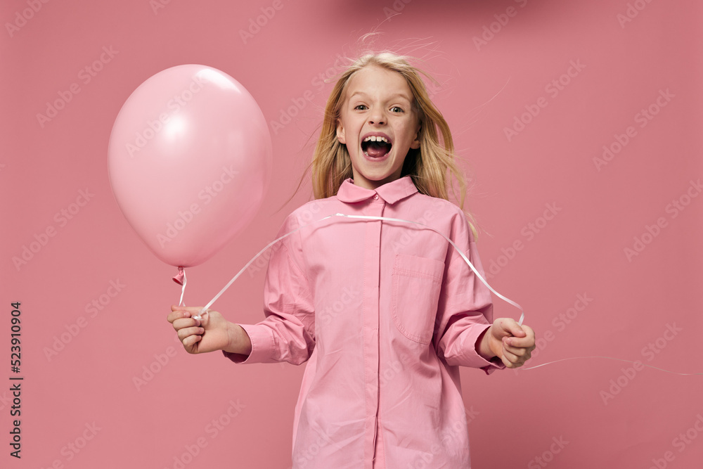 a beautiful, happy girl in a pink shirt stands on a pink background and smiling broadly at the camera holds a pink balloon in her hand a beautiful, happy girl in a pink shirt stands on a pink background and smiling broadly at the camera holds a pink balloon in her hand